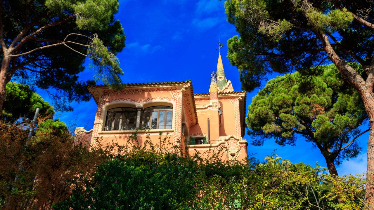 The Gaudí House Museum, the pink house with a gallery and a spire topped with a cross, where Antoni Gaudí lived, located among the pine trees in Park Güell