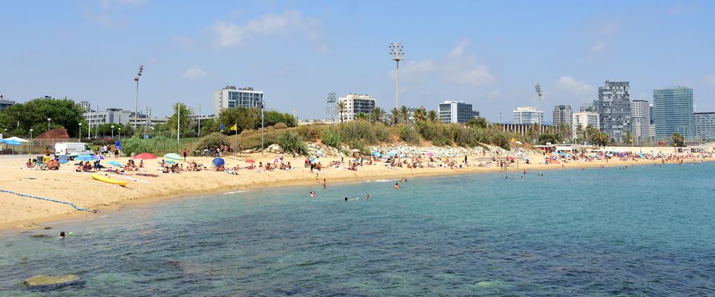 La playa del Bogatell de Barcelona vista desde el agua, con bañistas en la arena y las torres del frente marítimo al fondo