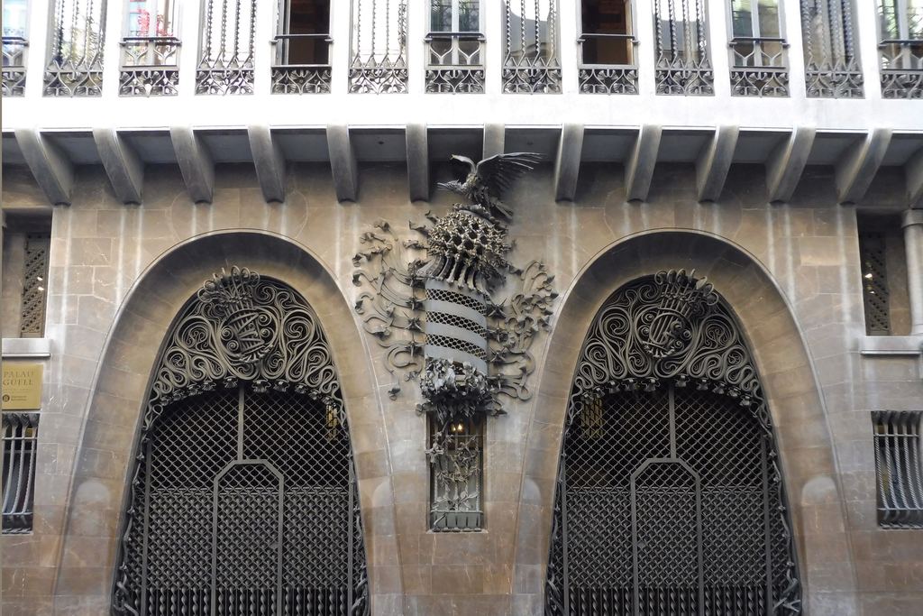 Fachada del Palau Güell en la calle Nou de la Rambla, con los dos arcos parabólicos de entrada y el escudo de Cataluña de hierro forjado entre ellos