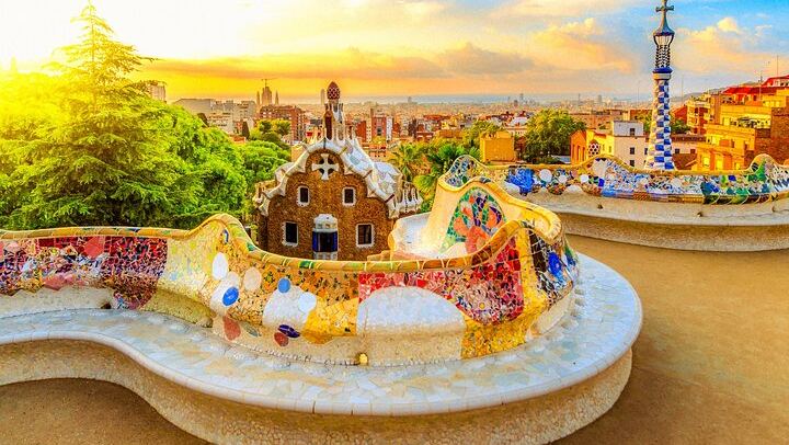 Relájese en el famoso banco serpenteante del Park Güell, enmarcado por vibrantes mosaicos y el horizonte de Barcelona.